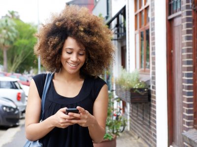 Happy black woman walking and reading text message